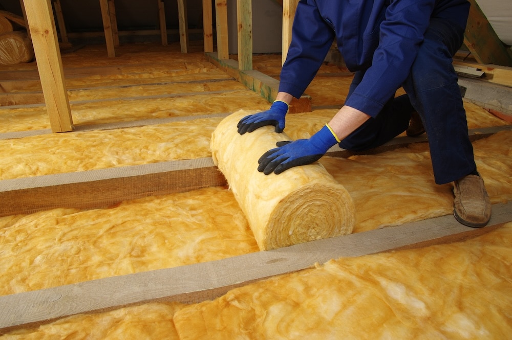 Worker applying fiberglass insulation down in attic of home